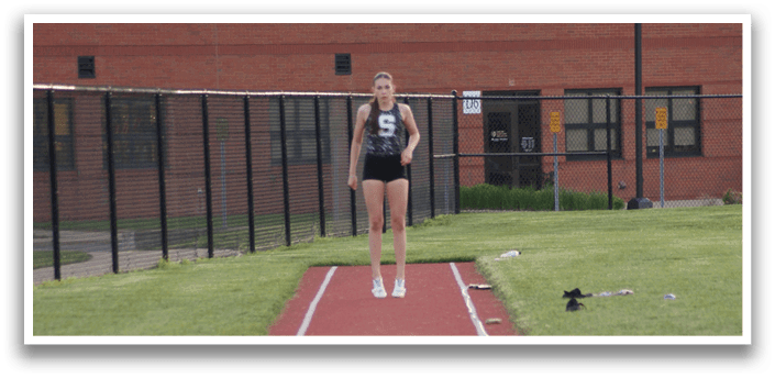 A woman is standing on a track, wearing a black shirt and shorts. She is holding a pole in her hand. Contenido generado con IA