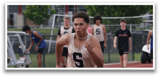 A group of people are running on a track, with one man wearing a gold shirt and the number 5. Contenido generado con IA