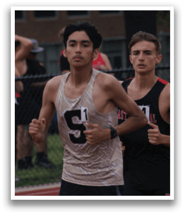 Three men are running on a track, wearing black shirts and shorts. They are in the middle of a race, with one man leading the pack. Contenido generado con IA