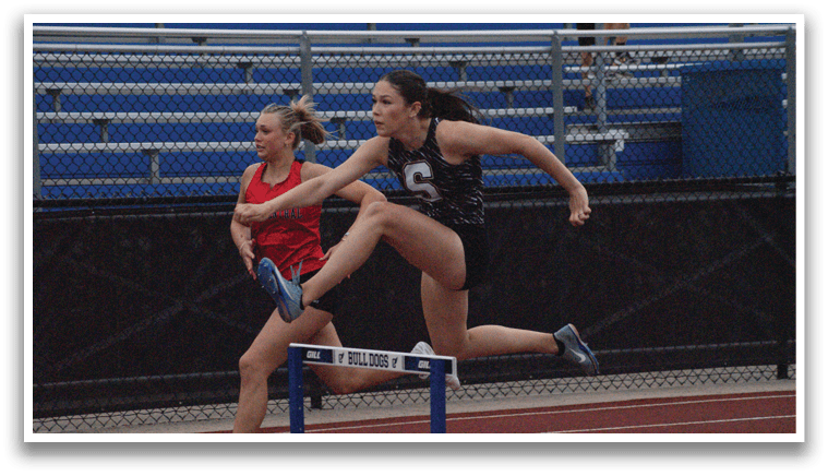 Two female athletes are running on a track, one of them jumping over a hurdle. Contenido generado con IA