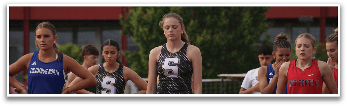 A group of female athletes wearing uniforms are standing on a track, waiting for the starting gun. Contenido generado con IA