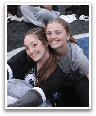 Two girls are sitting on the ground, smiling and posing for a picture. Contenido generado con IA