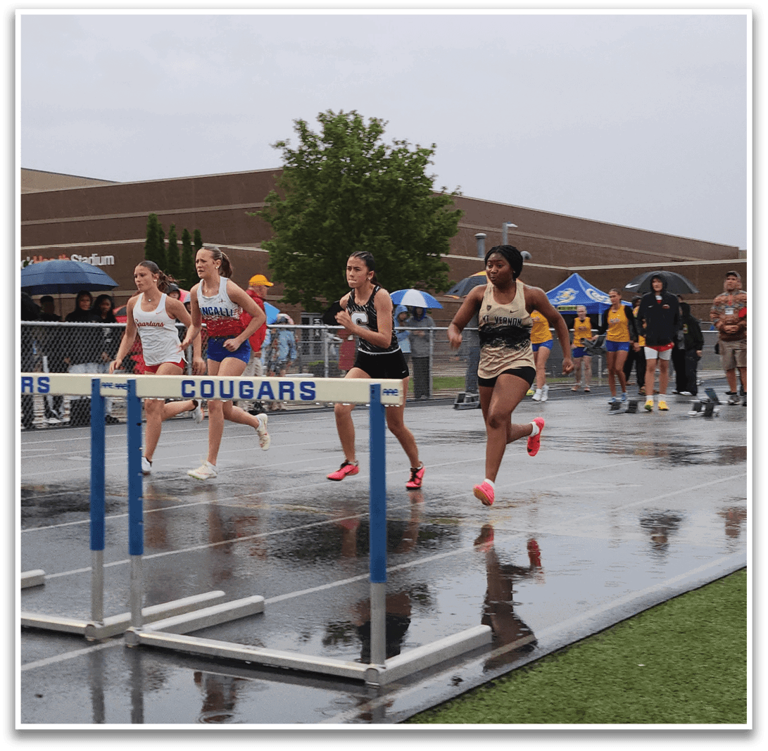 A group of women are running on a track, with one of them wearing a red shirt. They are running in front of a blue and white barrier. Contenido generado con IA