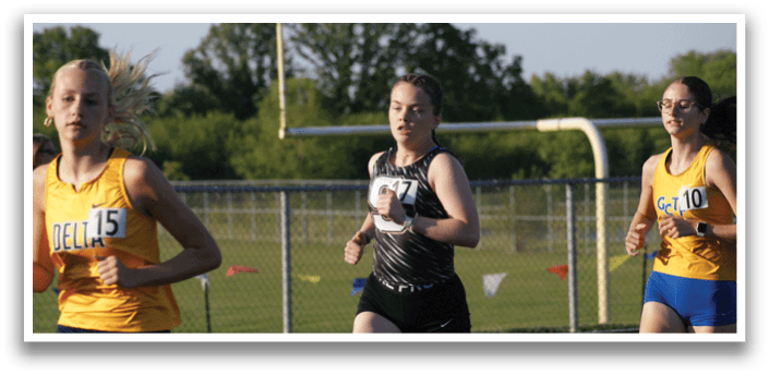 Three female runners wearing numbers on their shirts are running on a track. Contenido generado con IA