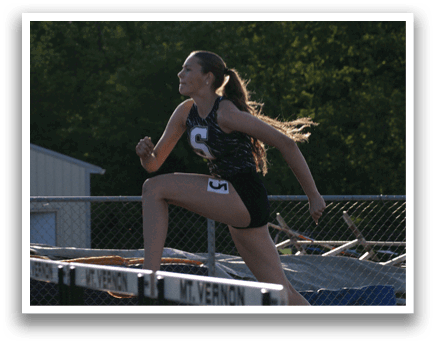 A female athlete is running on a track, wearing a black and white outfit. She is in the process of jumping over a hurdle. Contenido generado con IA