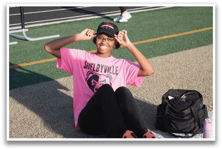 A woman wearing a pink shirt is sitting on the ground with her legs crossed. Contenido generado con IA