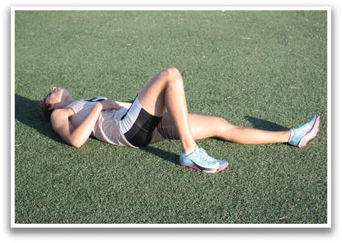 A woman is lying on the grass, wearing a tank top and shorts. She has her legs crossed and is resting on her stomach. Contenido generado con IA
