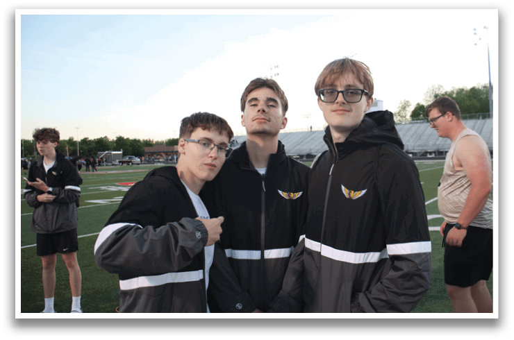 Three young men wearing black jackets and glasses pose for a picture on a field. Contenido generado con IA