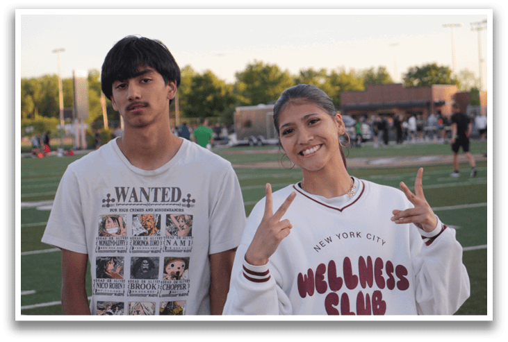 Two people standing on a field, one is wearing a white shirt with the word “wanted" on it and the other is wearing a white sweatshirt with the word "mellowness" on it. Contenido generado con IA