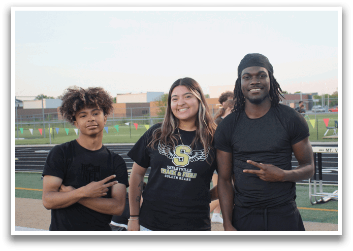 Three people are standing on a track, posing for a picture. They are wearing black shirts and pants. Contenido generado con IA
