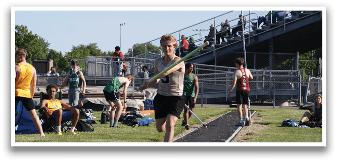 A man is holding a pole and standing on a track, preparing to throw it. There are several other people in the background, some of whom are also holding poles. Contenido generado con IA