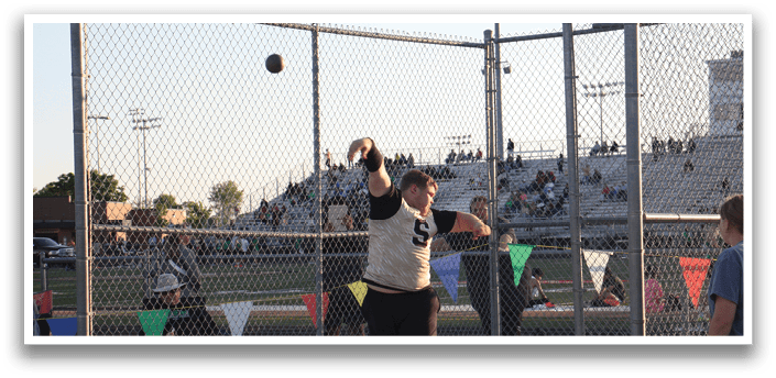 A man is throwing a ball in a fenced area, with a crowd of people watching. Contenido generado con IA