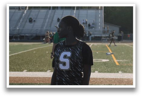 A woman wearing a black and white shirt stands on a football field. Contenido generado con IA