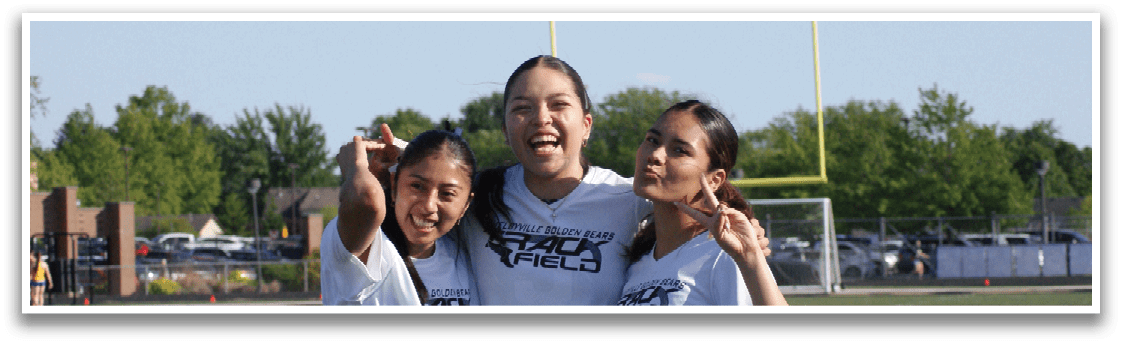 Three women wearing white shirts and black shorts pose for a photo on a football field. Contenido generado con IA