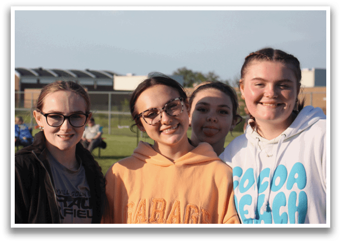 Three girls wearing glasses pose for a picture in front of a crowd. Contenido generado con IA