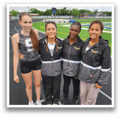 Four women are standing on a track, posing for a picture. They are wearing track suits and are all smiling. Contenido generado con IA