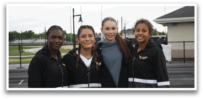 Four young women wearing black jackets and white shirts pose for a picture on a track. Contenido generado con IA