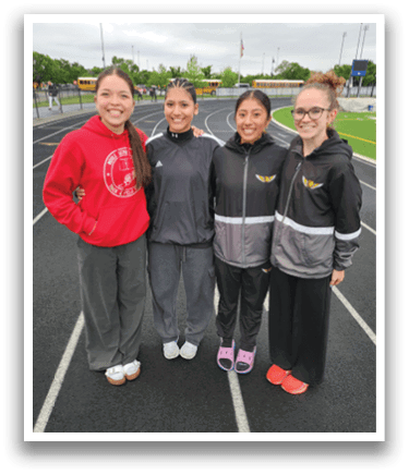 Four women wearing black and grey jackets pose for a picture on a track. Contenido generado con IA