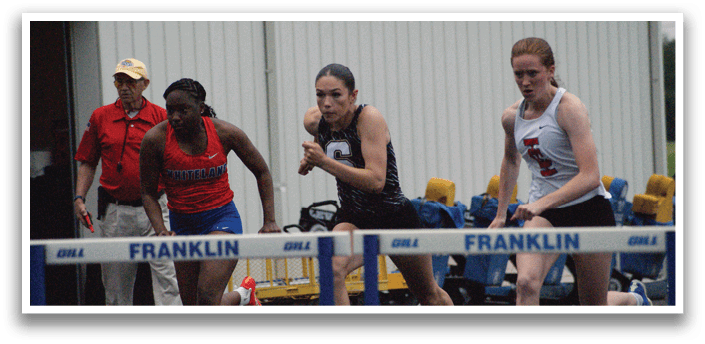 Two female runners are racing each other on a track, with one runner wearing a red shirt and the other wearing a black shirt. They are both running towards a blue and white barrier. A man in a red shirt is watching the race from behind. Contenido generado con IA
