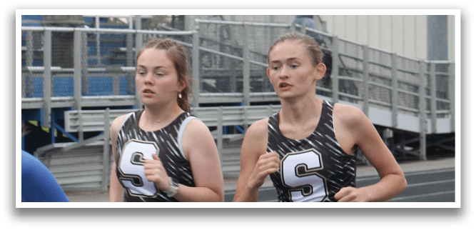 Three girls running on a track, wearing shorts and sprinting towards the finish line. Contenido generado con IA