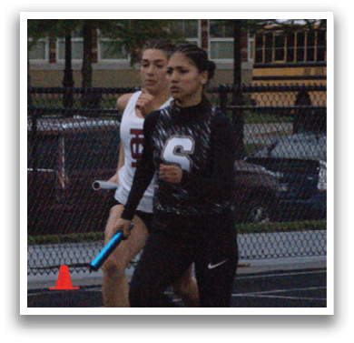 Three girls are running on a track, one wearing a green shirt, another wearing a black shirt, and the third wearing a white shirt. They are all running in the same direction. Contenido generado con IA