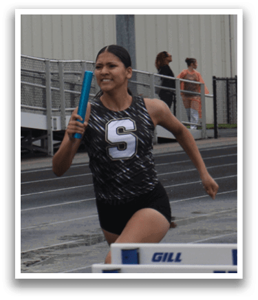 A female athlete is running on a track, wearing a black and white uniform. She is in the process of jumping over a hurdle. Contenido generado con IA