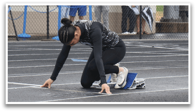 A woman is kneeling on a track, holding her skateboard. Contenido generado con IA