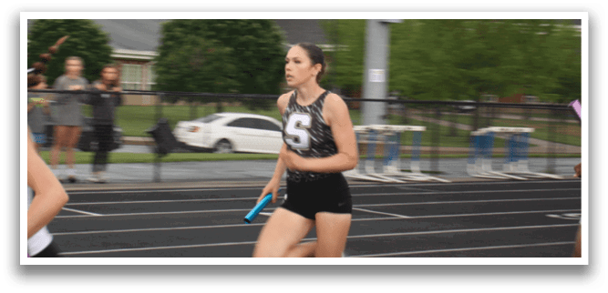 Two women are running on a track, one wearing a black and white outfit and the other wearing a black and white and black outfit. They are both holding pink and blue glow sticks. Contenido generado con IA