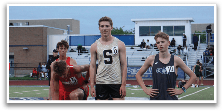 Three male runners are standing on a track, one of them is bent over. They are wearing shorts and are in the middle of a competition. Contenido generado con IA