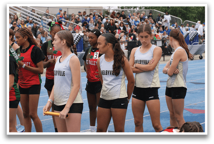 A group of female athletes wearing shorts and tank tops are standing on a track. Contenido generado con IA