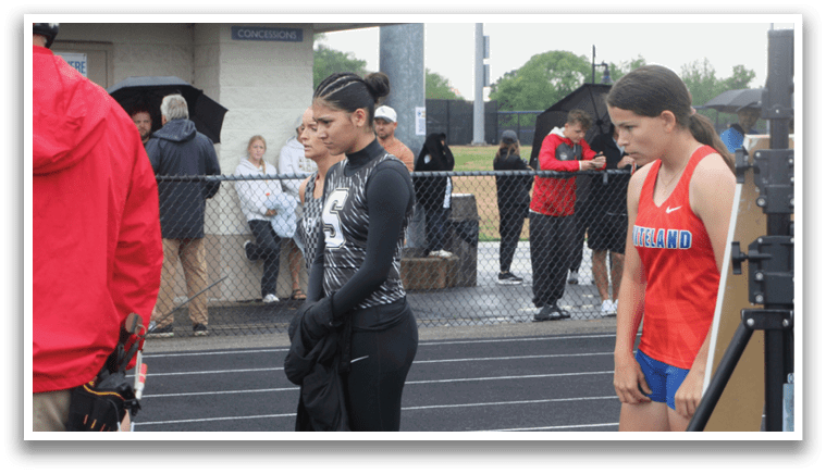 Two girls and a man are standing on a track. One girl is wearing a red shirt and the other is wearing a black shirt. The man is wearing a red jacket. Contenido generado con IA