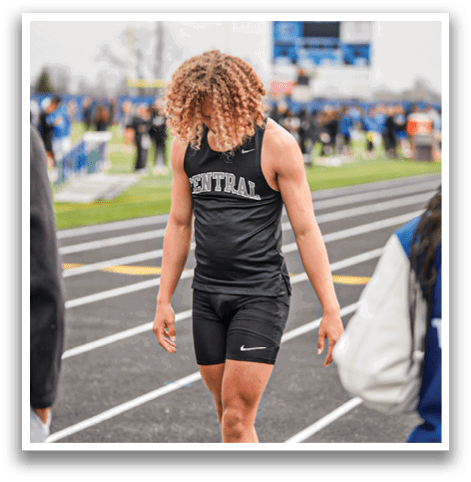 A man wearing a black and white shirt and black shorts is standing on a track. Description generated by AI