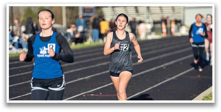 Two girls running on a track. Description generated by AI