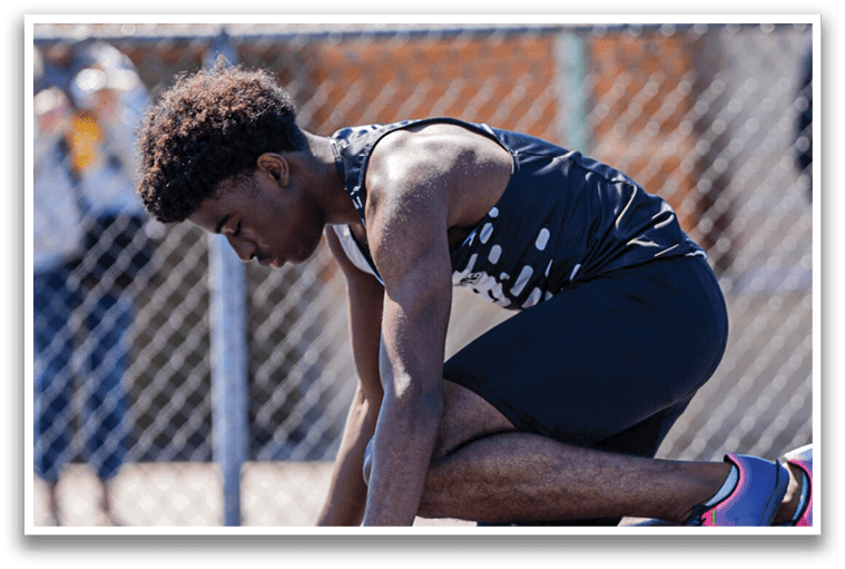A man is kneeling on a track with a pole in his hand. Description generated by AI