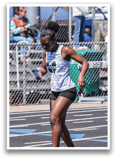 A woman wearing a white shirt and black shorts is running on a track. Description generated by AI