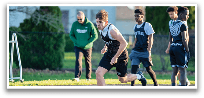 A man running on a track with other men behind him. Description generated by AI