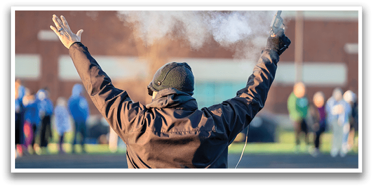 A man wearing a black hat and jacket is standing on a track with his arms raised. Description generated by AI