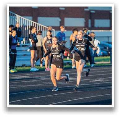 Two girls running on a track. Description generated by AI