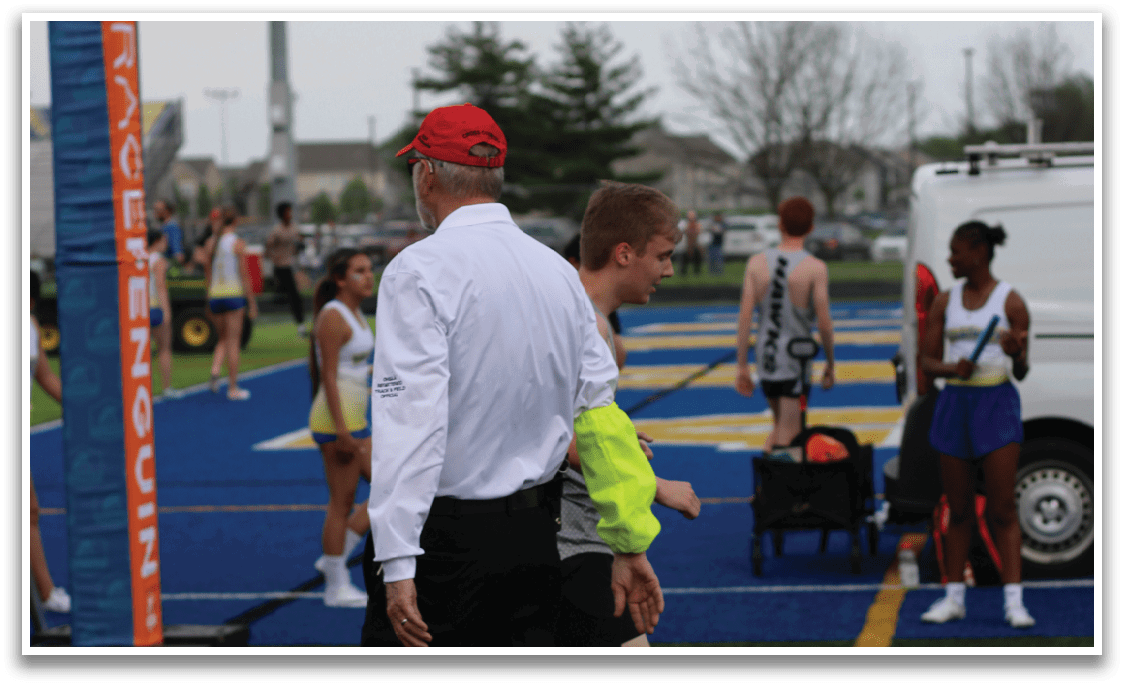A man wearing a white shirt and red hat is talking to another man. Description generated by AI