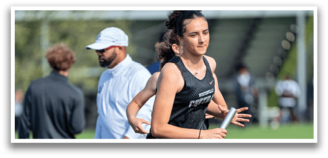 A woman running in a field with a man walking behind her. Description generated by AI