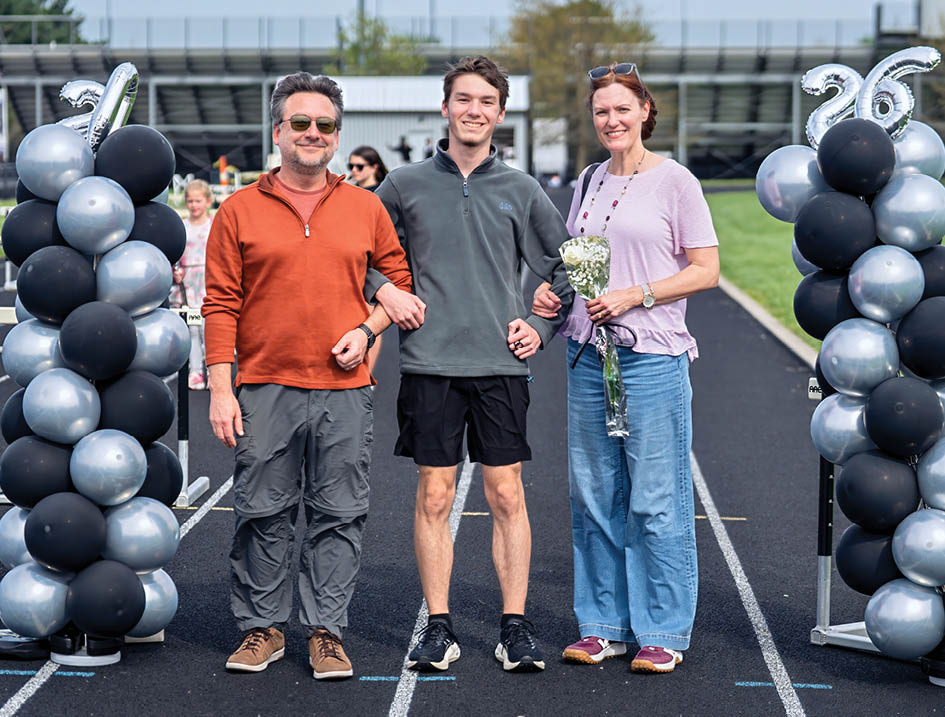 A man, woman, and child are standing in front of a banner. Description generated by AI