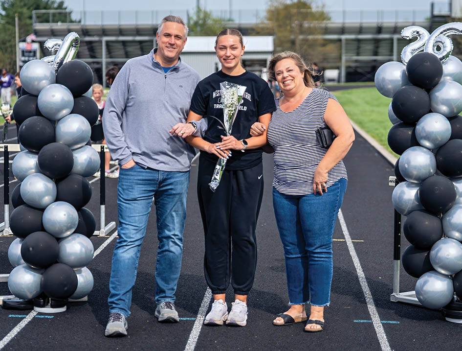 A man, woman, and girl are standing in front of a banner. Description generated by AI