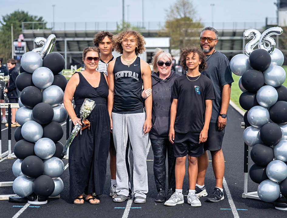 A group of people standing in front of a black and silver banner. Description generated by AI