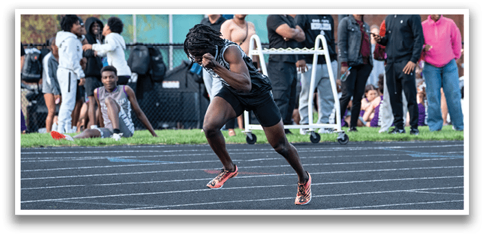 A man running on a track with a crowd of people watching. Description generated by AI