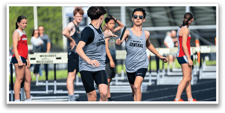 A boy in a grey shirt and black shorts is running on a track. Description generated by AI