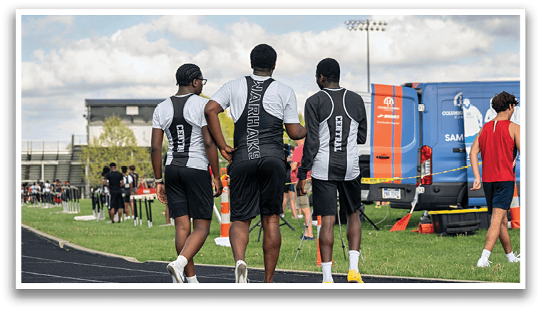 Three men walking on a track. Description generated by AI