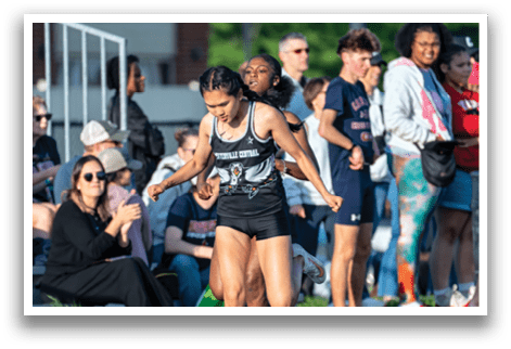 A woman running on a track with a crowd of people watching. Description generated by AI