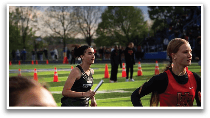 A woman running on a track with a black shirt and a white headband. Description generated by AI