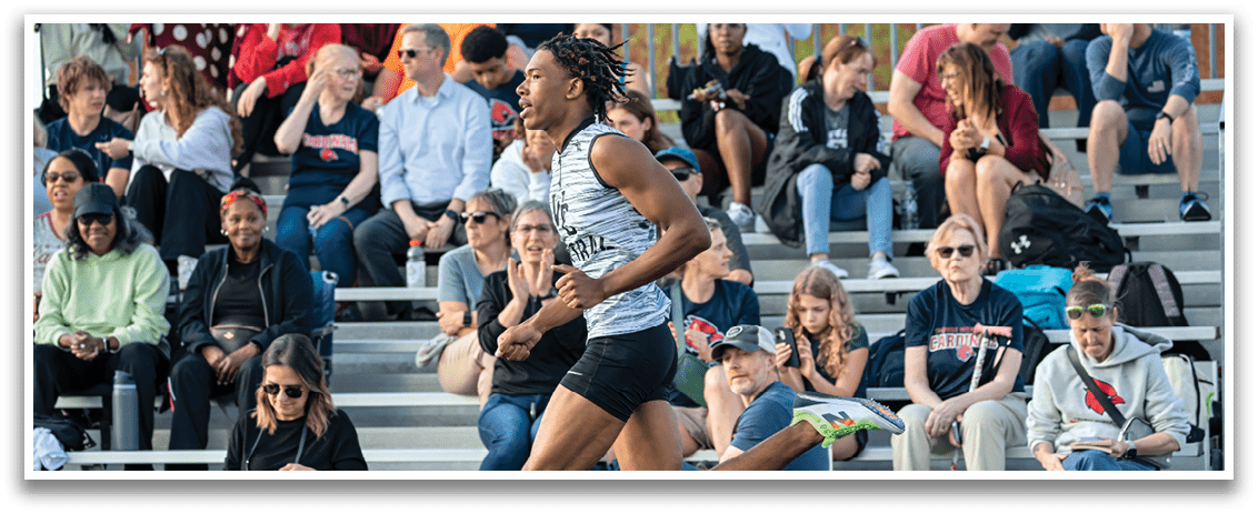 A man running on a track with a crowd watching. Description generated by AI