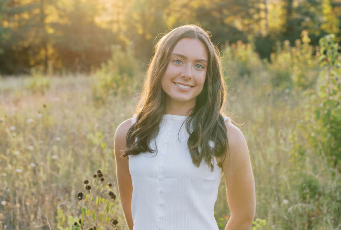 A woman in a white shirt and blue jeans standing in a field. Description generated by AI